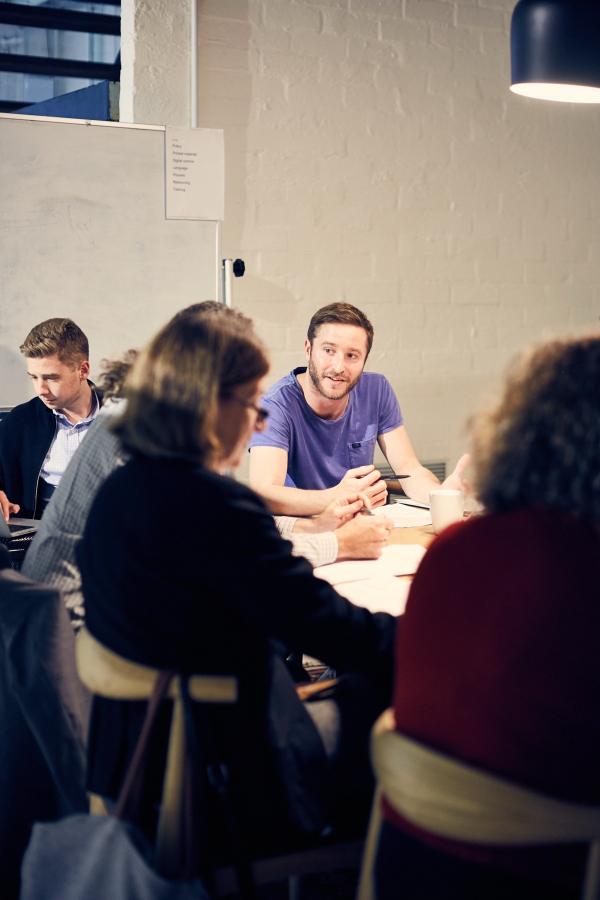 Mark at a long table in a brick-walled studio, talking through findings with a group of clients.